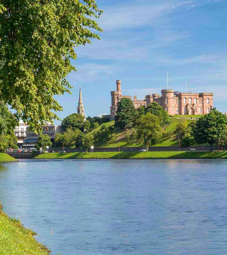 Blue sky as a castle sits on the hill behind a flowing river.