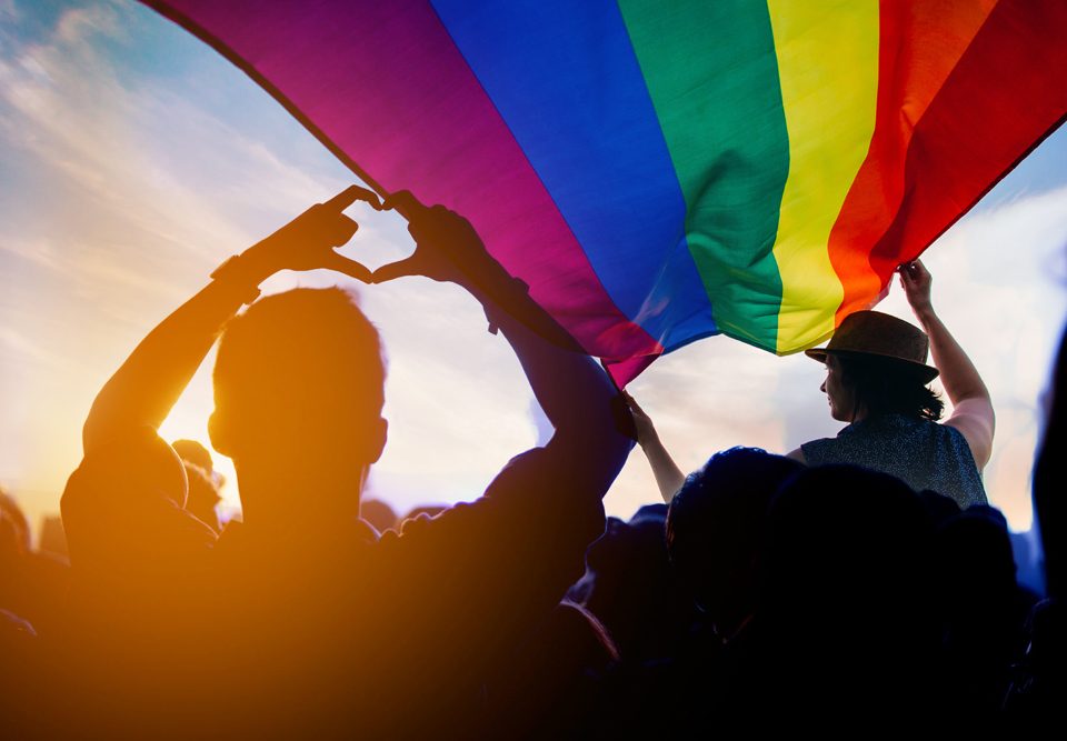 People holding the LGBT+ flag at a Pride event