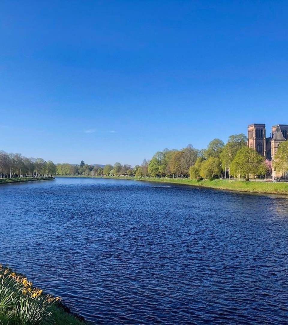 Inverness riverside with blue skies, daffodils and the cathedral visible through trees