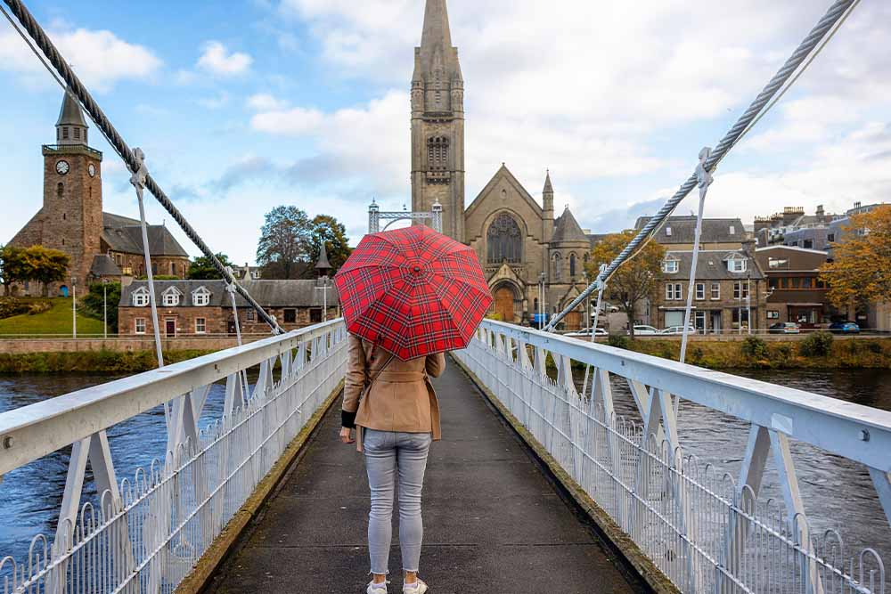 A person on a bridge in Inverness with an umbrella.