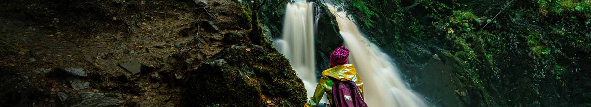 A person in a yellow jacket admires Plodda Falls in the highlands.