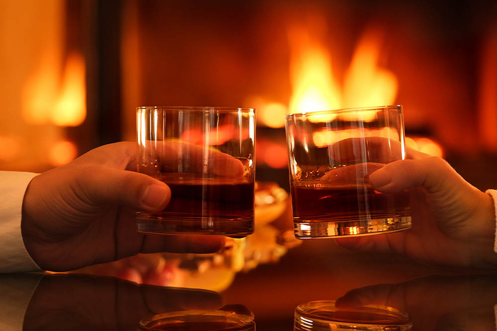 Clinking whisky glasses by a fire.